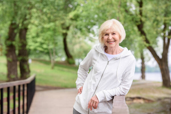 smiling senior woman standing near railings in park