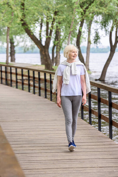 smiling senior woman walking on wooden path in park