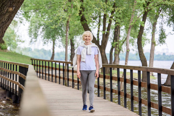 senior woman in sportswear walking on wooden path in park