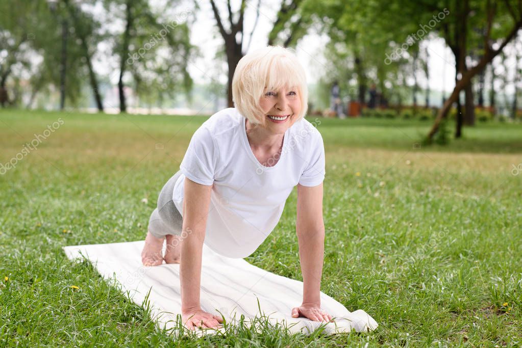 smiling elderly woman doing plank on yoga mat on lawn