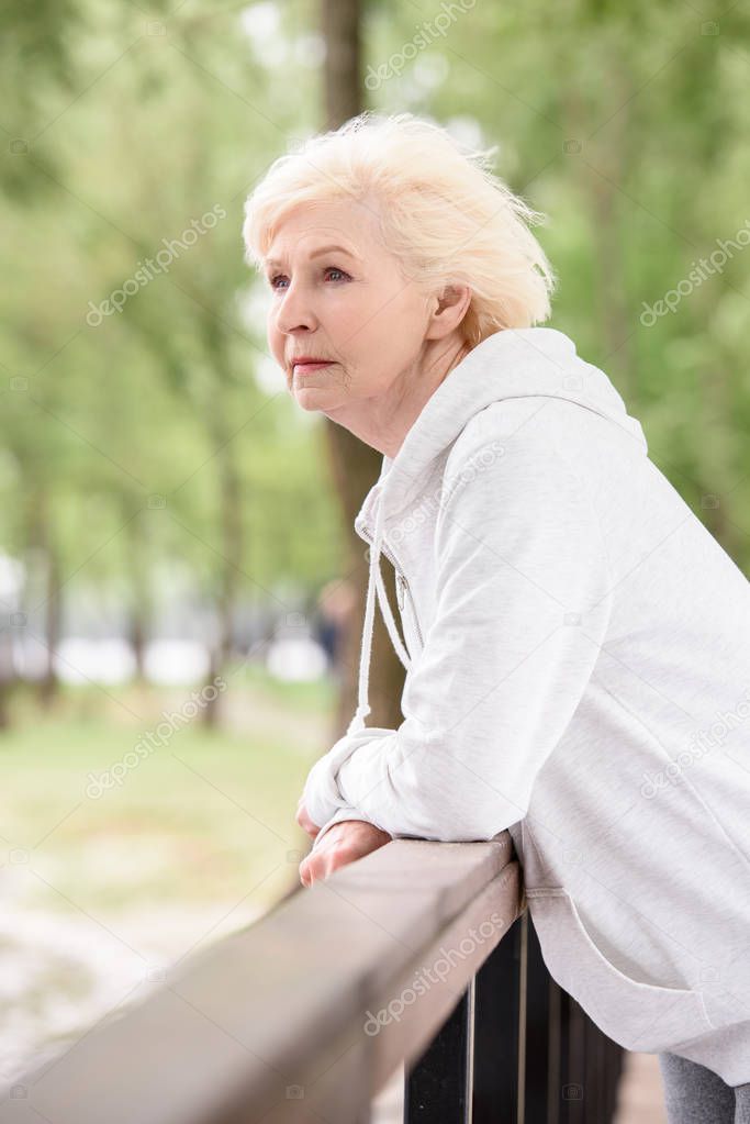 elderly woman standing near railings in park