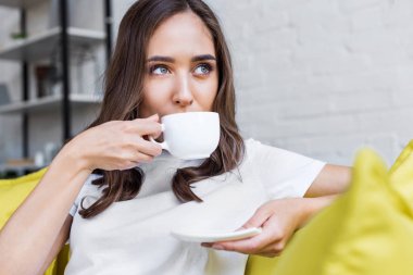 beautiful pensive brunette girl drinking coffee and looking away at home clipart