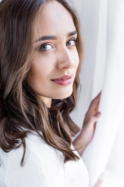 Beautiful Brunette Girl Touching Curtain Looking Camera — Stock Photo, Image