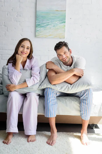 若いパジャマ枕とベッドの上に座ってカップルの笑顔 — ストック写真