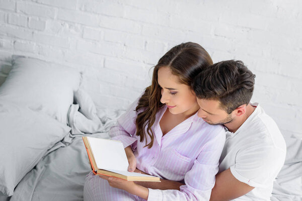 young couple hugging and reading book together in bed
