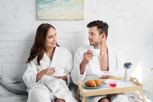 年轻夫妇在浴袍早餐在床上早上 — 免费的图库照片