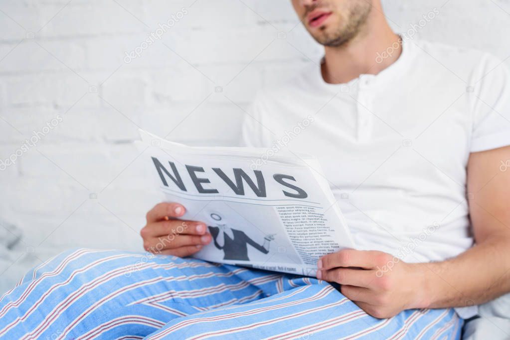 cropped view of man in pajamas reading newspaper at home in morning