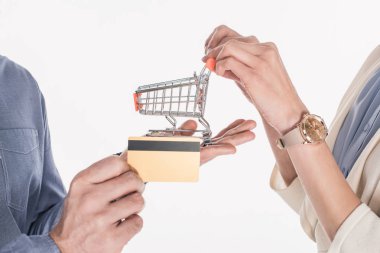 cropped shot of couple holding little shopping cart and credit card in hands isolated on white