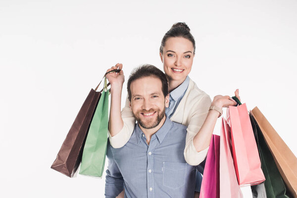 happy woman with shopping bags and husband piggybacking together isolated on white