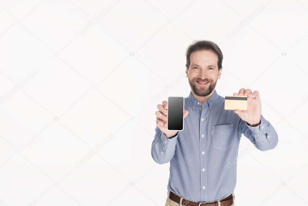 portrait of smiling bearded man showing smartphone with blank screen and credit card in hands isolated on white