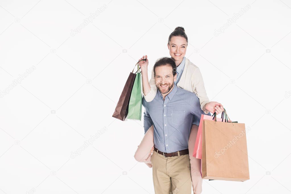 happy woman with shopping bags and husband piggybacking together isolated on white