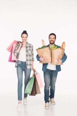 cheerful wife and husband carrying shopping bags and paper packages full of food isolated on white
