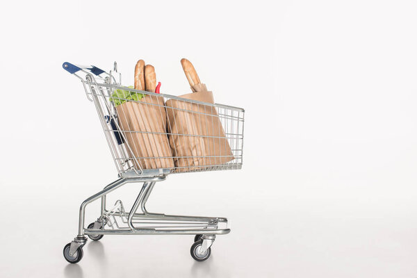 close up view of shopping cart with paper packages full of grocery isolated on white