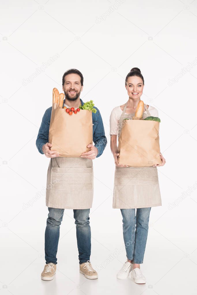 cheerful shop assistants in aprons holding paper packages with food isolated on white