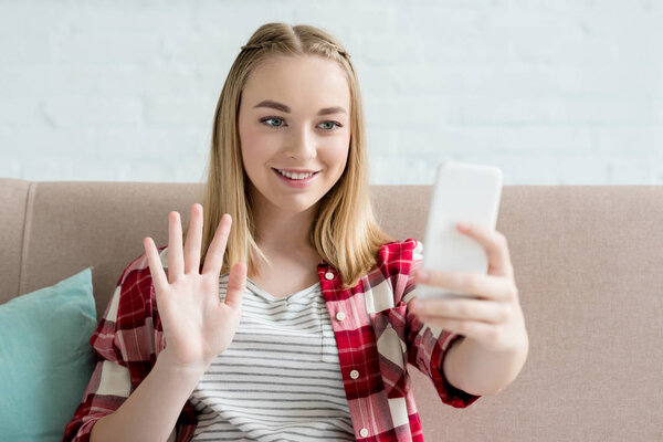 close-up portrait of teen student girl making video call with smartphone and waving at camera
