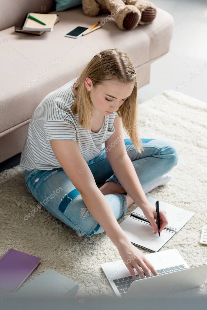 high angle view of teen student girl doing homework while sitting on floor