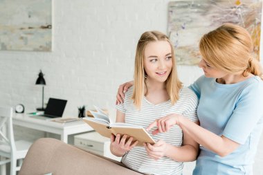 Anne ve genç kızı evde birlikte kitap okuma