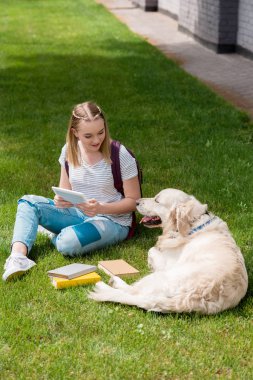 mutlu genç öğrenci kız köpeğini çim üzerinde otururken tablet kullanma