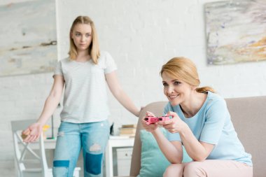 confused teen daughter looking at mother while she playing console game clipart