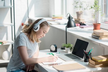 teen student girl listening music with headphones and doing homework clipart