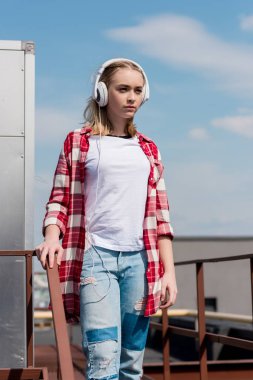 beautiful teen girl in red plaid shirt and headphones in front of blue sky clipart