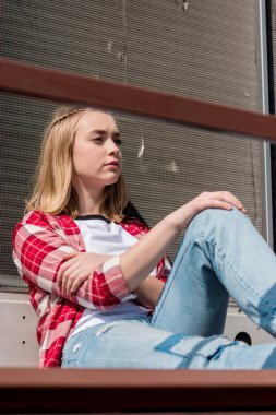 thoughtful teen girl in red plaid shirt sitting on rooftop clipart