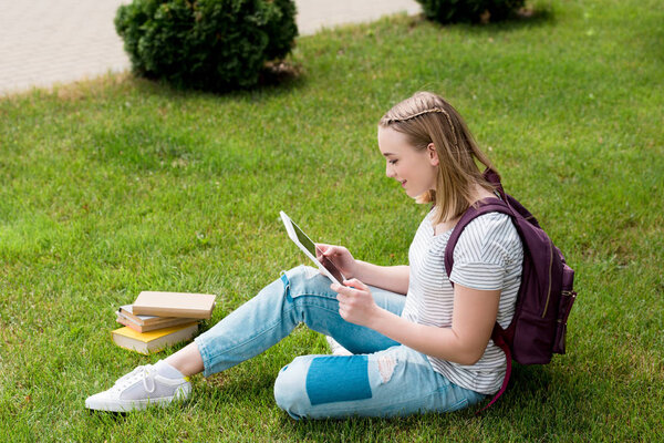 teen student girl using tablet while sitting on grass