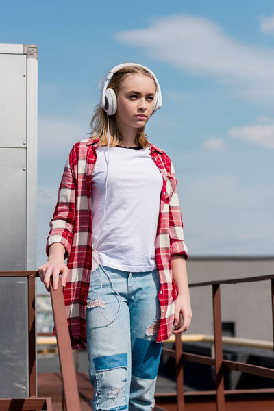 beautiful teen girl in red plaid shirt and headphones in front of blue sky