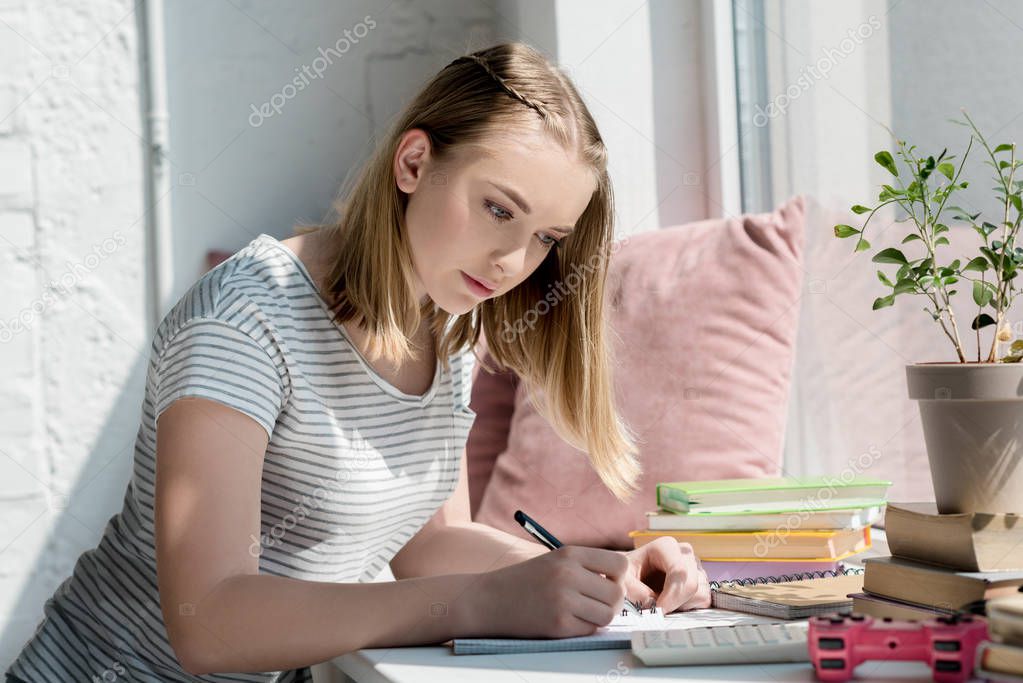 focused teen student girl doing homework on windowsill