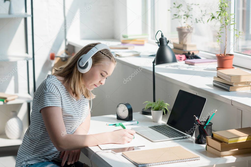 teen student girl listening music with headphones and doing homework