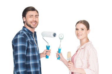 boya merdaneleri ve beyaz arka plan üzerinde izole boya fırçası ile gülümseyen genç çift 