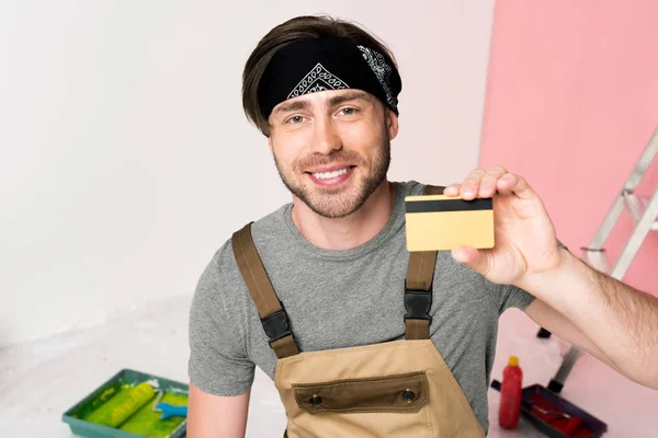 Lächelnder Mann Mit Stirnband Und Arbeitskleidung Mit Kreditkarte — kostenloses Stockfoto