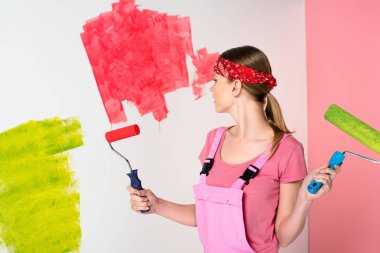kafa bandı ve çalışma boya merdaneleri boyalı duvar önünde tutan genel genç kadın