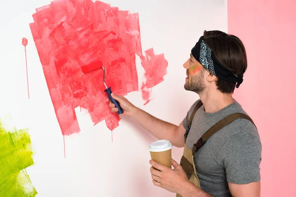 ペイント ローラーで赤でコーヒー カップの絵壁を持つ男を笑顔の側面図  — 無料ストックフォト