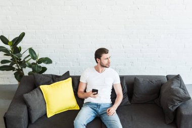evde el smartphone ile kanepede oturan genç adam görünümünü yüksek açı 