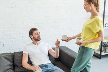 Genç kadın erkek kanepe evde kahve fincanı veren gözlük yan görünüm