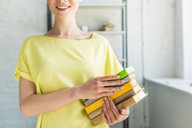 cropped image of smiling young woman holding stack of books