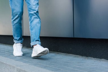 partial view of stylish male legs in jeans and white sneakers on asphalt  clipart