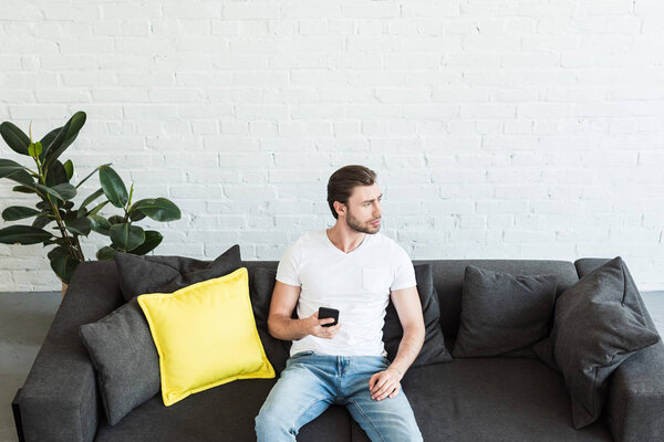 high angle view of young man sitting on sofa with smartphone in hand at home 