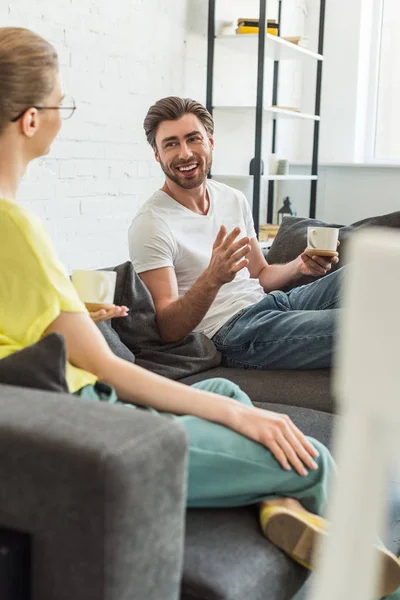 Junges Lächelndes Paar Mit Kaffeetassen Gespräch Und Auf Dem Heimischen — kostenloses Stockfoto