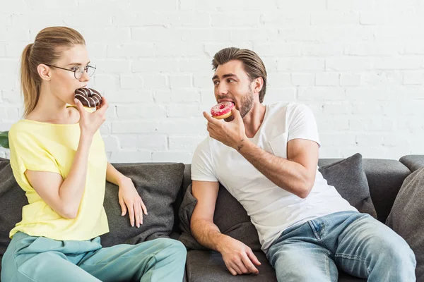 Young Couple Eating Donuts Sitting Sofa Home — Free Stock Photo