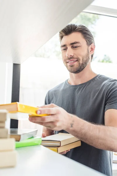 Jovem Sorrindo Homem Colocando Livros Prateleiras Casa — Fotografia de Stock