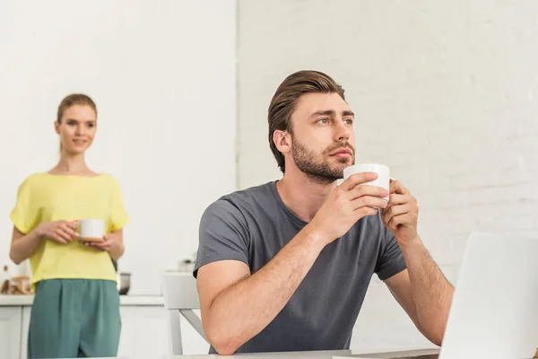 Nadenkende Jongeman Zitten Met Een Koffiekopje Aan Tafel Met Laptop — Gratis stockfoto