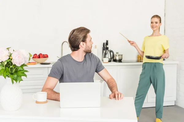 Young Man Working Table Laptop His Girlfriend Standing Frying Pan — Free Stock Photo