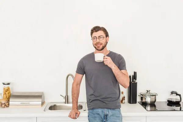 Čelní Pohled Úsměvem Mladý Muž Brýlích Pití Kávy Kuchyni — Stock fotografie