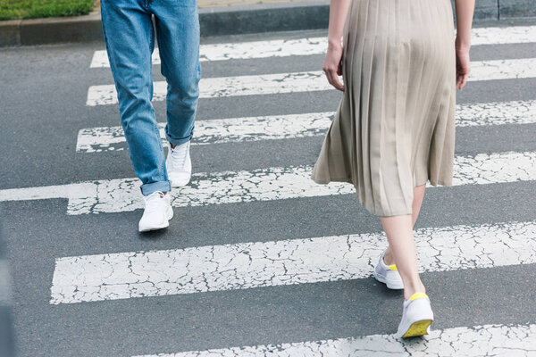 cropped image of stylish man in jeans and woman in long skirt walking on crosswalk 