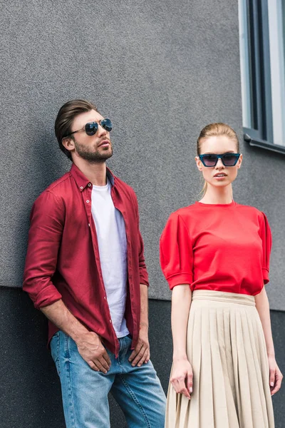 stylish young couple of models in sunglasses posing near building