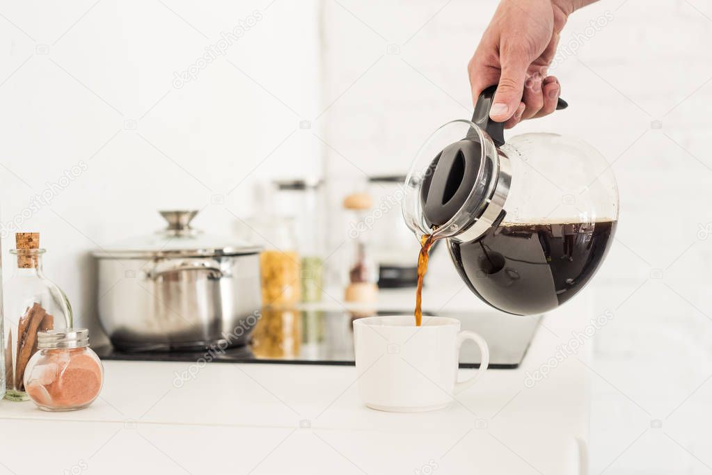 cropped image of man pouring coffee into cup from coffee maker at kitchen  
