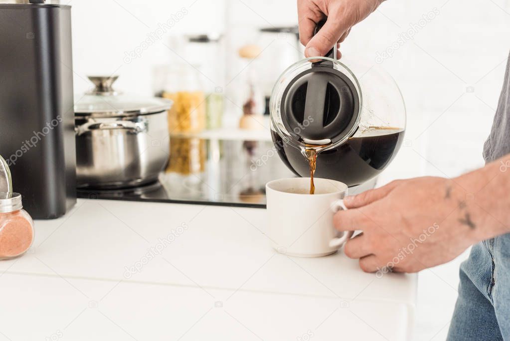 partial view of man pouring coffee into cup from coffee maker at kitchen  