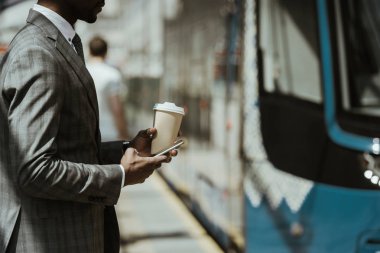 Trenle smartphone ve kahve Kupası ile genç Afro-Amerikalı işadamı kırpılmış görünümü